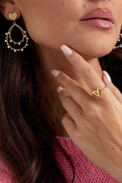 Złote kolczyki i pierścionek serce na kobiecie.